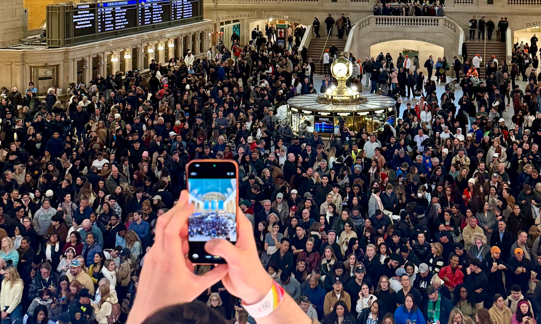 Auto-generated description: A large crowd fills Grand Central Terminal, with someone in the foreground taking a photo of the bustling scene.