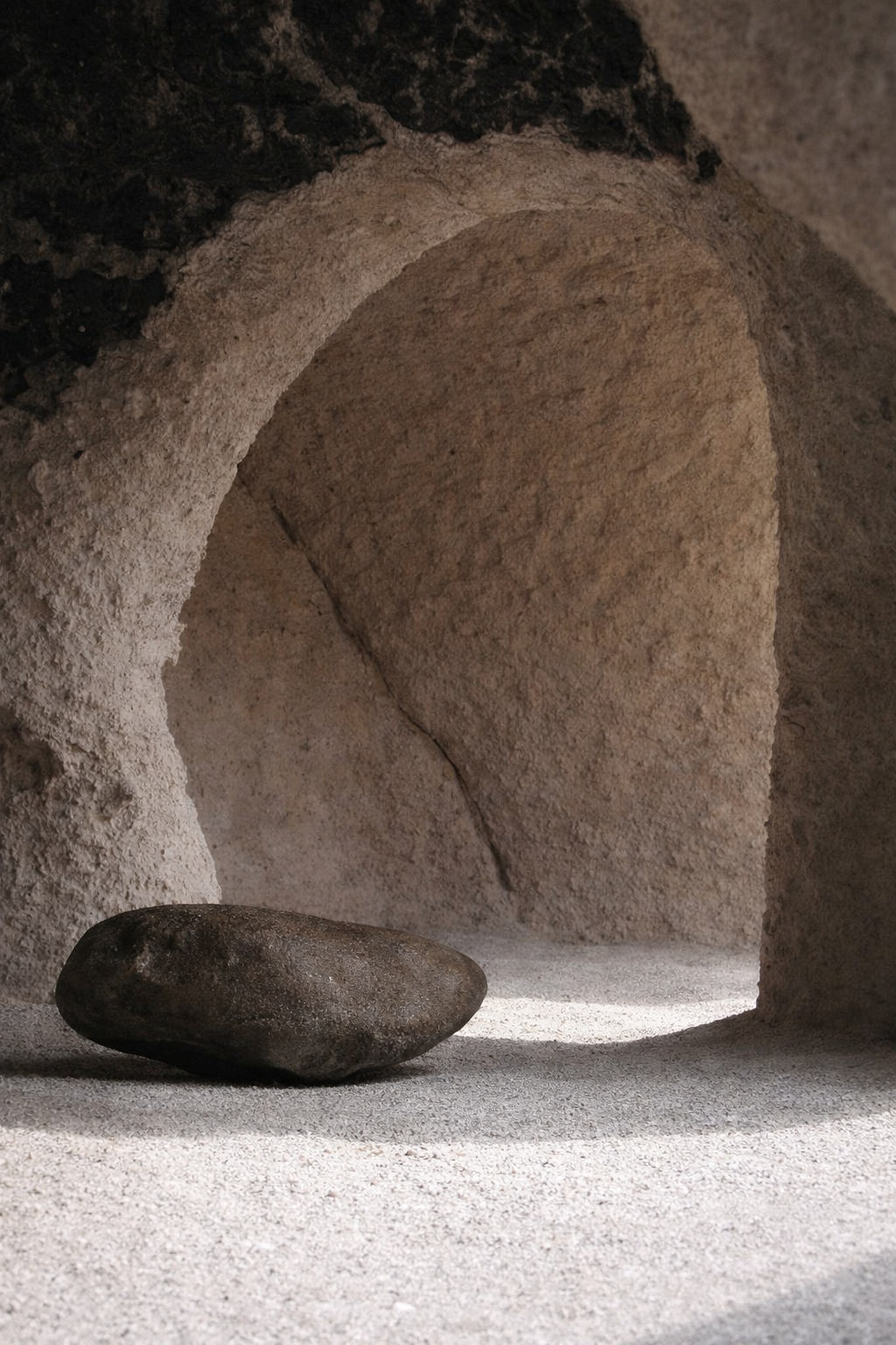 A large rock rests on a sandy surface inside a curved, cave-like structure.