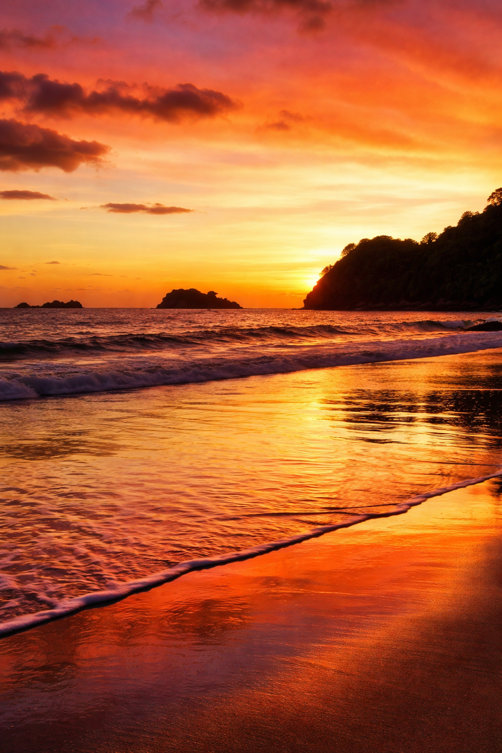 A vibrant sunset casts warm hues over a tranquil beach and calm ocean waves.